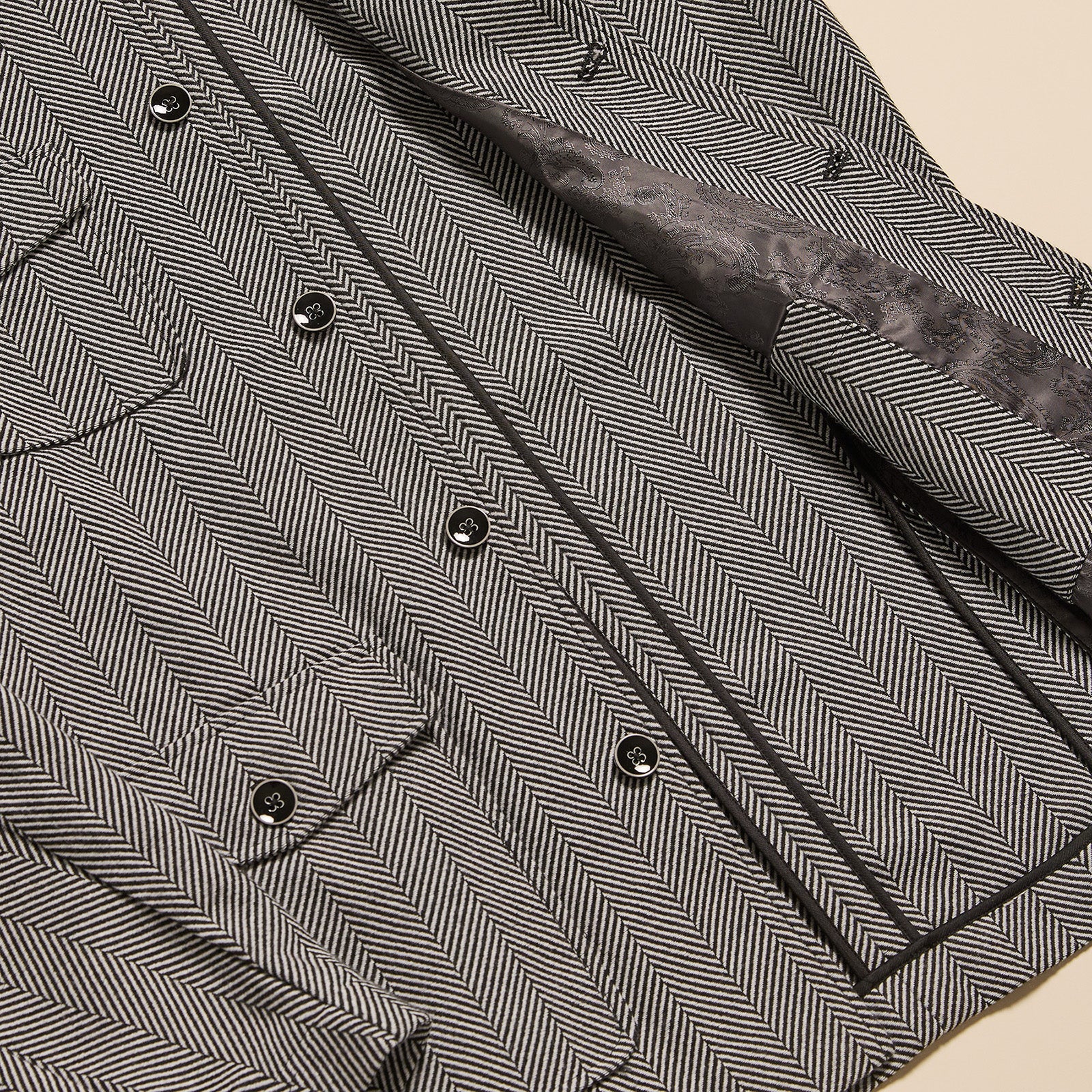 Close-up view of men’s herringbone 4 pocket jacket fabric with button detail in black and white pattern.
